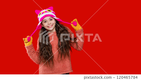 Happy girl in winter hat. Winter fashion style. Teenager knitted fashion. Outdoor lifestyle fashion. Teenager girl in a winter warm hat isolated on red. Copy space advertisement 120465784
