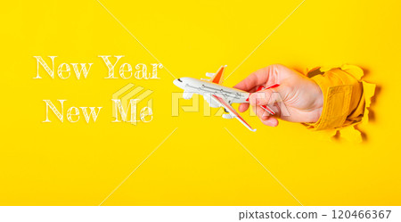 Hand holding a toy airplane with the words New Year Now Me written below it 120466367