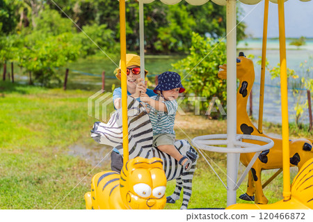 a little boy is a blonde child with his older brother in an amusement park, riding on a carousel, smiling, rejoicing a little boy is a blonde child with his older brother in an amusement park, riding on a carousel, smiling, rejoicing 120466872