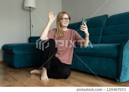 Hi. Female in glasses taking a selfie photo using her mobile phone at home. 30s woman in t-shirt recording self video, talking on online call and relaxing on floor near sofa Hi. Female in glasses taking a selfie photo using her mobile phone at home. 30s woman in t-shirt recording self video, talking on online call and relaxing on floor near sofa 120467053