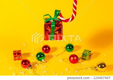 Candy cane lollipop holding a gift box with a Christmas present on a yellow background, Christmas sweets with new year decorations Candy cane lollipop holding a gift box with a Christmas present on a yellow background, Christmas sweets with new year decorations 120467407