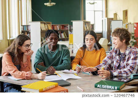 Group of students working together on assignments at table in library setting, creating an inclusive and collaborative environment for academic success, with textbooks and papers around 120467746