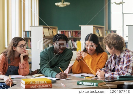 Group of high school students sitting at a table in bright library, engaging in a study session. Various textbooks on math subjects spread across table 120467748