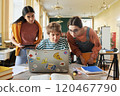 Three young professionals collaborating using laptop in bright, modern office. Diverse group engaging in discussion, sharing ideas, and planning project without eye contact with camera 120467790
