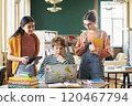 Three female students discussing study materials in library with books and laptop on table while engaging in collaborative learning session 120467794