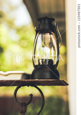 Black metal glass kerosene portable vintage retro lamp for outdoor lighting in night home garden. Decor for a backyard on light green natural backdrop Black metal glass kerosene portable vintage retro lamp for outdoor lighting in night home garden. Decor for a backyard on light green natural backdrop 120467801