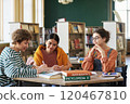 Group of students discussing work in library room filled with bookshelves and natural light coming through windows 120467810