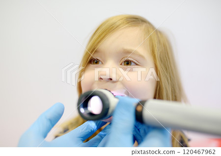 Cute little girl during appointment of dermatologist in modern clinic. Male doctor looking a pimple on a lips of child. Treatment of herpes virus, streptococcus infection 120467962