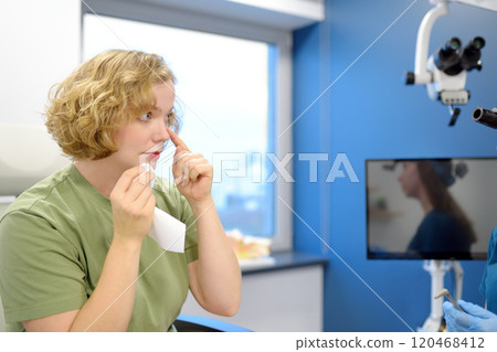 A young woman at an appointment with an otolaryngologist talks about her symptoms. A professional ENT doctor examines a patient. 120468412