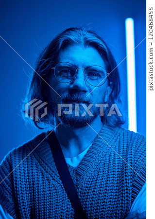 Portrait of bearded man with glasses in an atmospheric blue-toned setting, wearing a knitted sweater, presenting calm and thoughtful expression Portrait of bearded man with glasses in an atmospheric blue-toned setting, wearing a knitted sweater, presenting calm and thoughtful expression 120468458