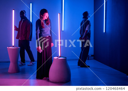 Individuals observing light sculptures in modern art gallery with neon blue and pink lighting creating an immersive, thoughtful environment 120468464