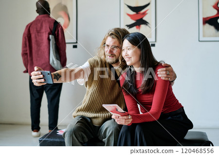 Smiling friends taking selfie in modern art gallery, enjoying artwork in background and capturing their memories sharing memorable moments together Smiling friends taking selfie in modern art gallery, enjoying artwork in background and capturing their memories sharing memorable moments together 120468556