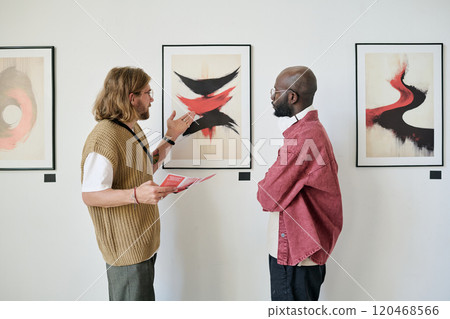Two men talking and analyzing abstract artwork in modern gallery setting. They are paying close attention to the details and discussing perspective techniques 120468566