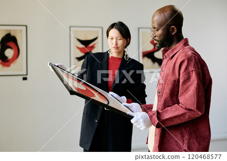Two individuals intently examining modern art pieces in a gallery setting with a focus on abstract paintings and captured during an engaging discussion Two individuals intently examining modern art pieces in a gallery setting with a focus on abstract paintings and captured during an engaging discussion 120468577