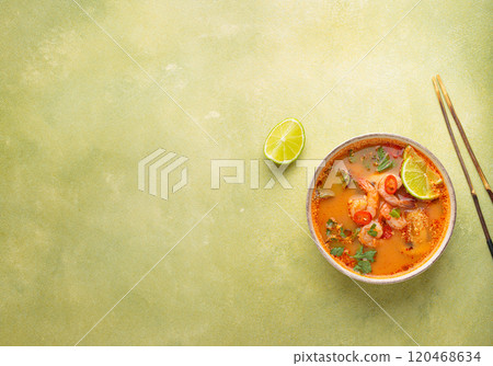 Tom yum soup with shrimps, lime, chili pepper and cilantro is served in bowl with chopsticks, traditional Thai cuisine Tom yum soup with shrimps, lime, chili pepper and cilantro is served in bowl with chopsticks, traditional Thai cuisine 120468634