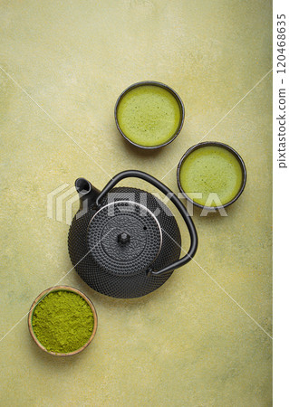 Matcha tea powder and hot drink in bowls with black iron teapot on green background, Japanese tea top view Matcha tea powder and hot drink in bowls with black iron teapot on green background, Japanese tea top view 120468635
