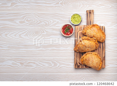 Delicious baked empanadas with sesame seeds served on wooden board with sauces, traditional Spanish savoury pastry Delicious baked empanadas with sesame seeds served on wooden board with sauces, traditional Spanish savoury pastry 120468642