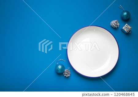 Empty plate surrounded by christmas ornaments on blue background for holiday menu or invitation 120468645