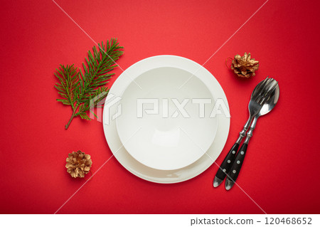 Christmas table setting with empty white plate, fir branch and golden pine cones on red background Christmas table setting with empty white plate, fir branch and golden pine cones on red background 120468652