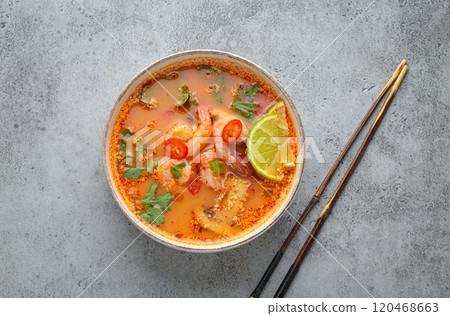 Spicy tom yum soup with shrimps, lime, chili pepper and coriander served in bowl top view, traditional Thai cuisine Spicy tom yum soup with shrimps, lime, chili pepper and coriander served in bowl top view, traditional Thai cuisine 120468663