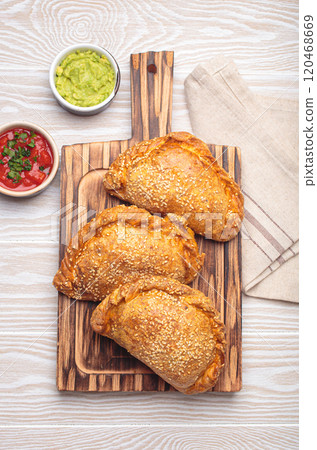 Delicious baked empanadas with sesame seeds served on wooden board with sauces, traditional Spanish savoury pastry 120468669