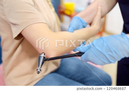 A woman at an appointment with a neurologist. A doctor examining elbow reflex of young female patient. A woman at an appointment with a neurologist. A doctor examining elbow reflex of young female patient. 120468687