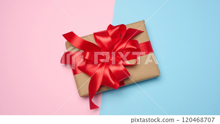 Box wrapped with red ribbon and brown craft paper on a pink blue background, top view Box wrapped with red ribbon and brown craft paper on a pink blue background, top view 120468707
