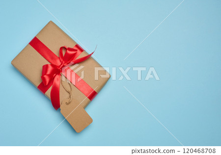 The box is wrapped with red ribbon and brown craft paper with a tag on a blue background The box is wrapped with red ribbon and brown craft paper with a tag on a blue background 120468708