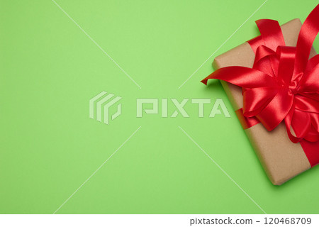 Box wrapped with red ribbon and brown craft paper on a green background, top view Box wrapped with red ribbon and brown craft paper on a green background, top view 120468709