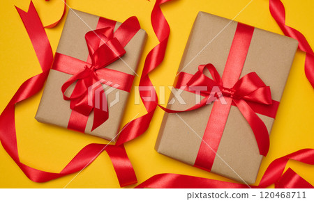 Two boxes tied with red ribbon on yellow background, festive background. 120468711