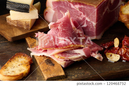 A piece of prosciutto, slices of ciabatta and cheese on a wooden board 120468732