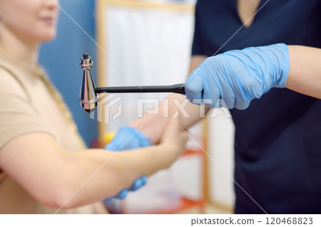 A woman at an appointment with a neurologist. A doctor examining elbow reflex of young female patient. 120468823