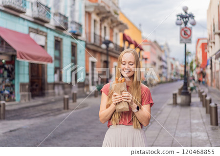 Female tourist eating churros on a colonial street in Puebla, Mexico. Cultural experience, local cuisine, and street food exploration concept 120468855
