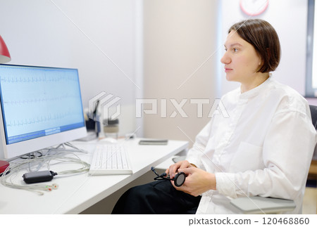 A cardiologist during appointment of patient. Doctor shows EKG on the screen of computer and explains about deviations of heart work. Cardiology consultation and treatment A cardiologist during appointment of patient. Doctor shows EKG on the screen of computer and explains about deviations of heart work. Cardiology consultation and treatment 120468860