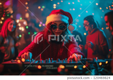 Female dj wearing a santa hat is mixing music at a christmas party, with people dancing in the background 120469824