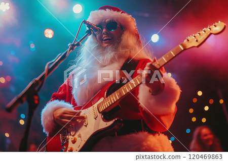 Female musician wearing a santa claus costume is playing an electric guitar and singing in a microphone on stage during a christmas concert 120469863