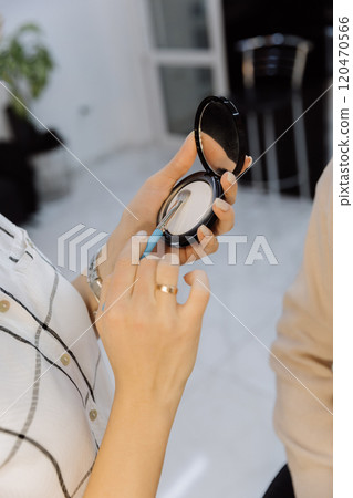 Close up of hands using a makeup brush and compact powder in a professional beauty setup 120470566