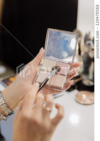 Makeup artist using a brush to apply highlighter from a compact palette for a radiant glow 120470568