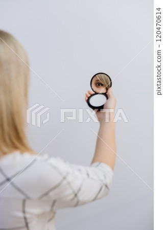 Reflection of a womans eye in a handheld compact mirror against a minimal background. 120470614