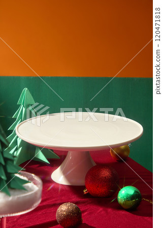 A large white presentation tray placed on red table, sparkling balls and green pine decorated around. Front view on green and orange background, space for adding text 120471818