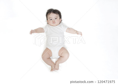 Aerial shot of a baby wearing a white romper lying on his back and looking at the camera 120471975