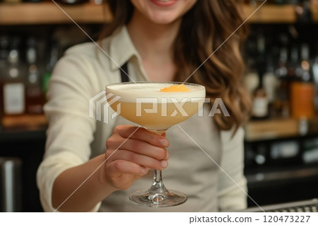 A woman is holding a glass of a drink with a slice of orange in it A woman is holding a glass of a drink with a slice of orange in it 120473227
