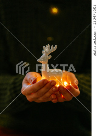 Warm festive Christmas image of hands holding deer ornament. Ceramic deer figurine in warm Christmas light held by a woman hands 120473502