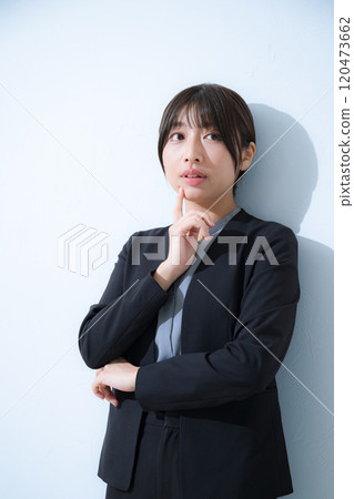 Business scene of a young woman wearing a suit thinking with her hand on her chin, light blue background, vertical of a woman worried about changing jobs or job hunting Business scene of a young woman wearing a suit thinking with her hand on her chin, light blue background, vertical of a woman worried about changing jobs or job hunting 120473662