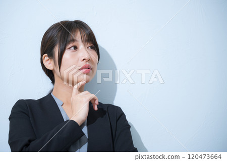 在淺藍色背景中,一位憂心忡忡的年輕女子穿著西裝,手放在下巴上思考的商業場景 在淺藍色背景中,一位憂心忡忡的年輕女子穿著西裝,手放在下巴上思考的商業場景 120473664