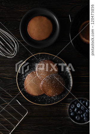 Chocolate pancakes on plates, bowl with berries on wooden background, top view 120473856