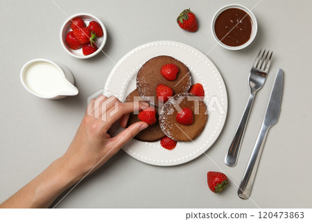 Chocolate pancakes on plate, strawberries, chocolate and hand on gray background, top view Chocolate pancakes on plate, strawberries, chocolate and hand on gray background, top view 120473863