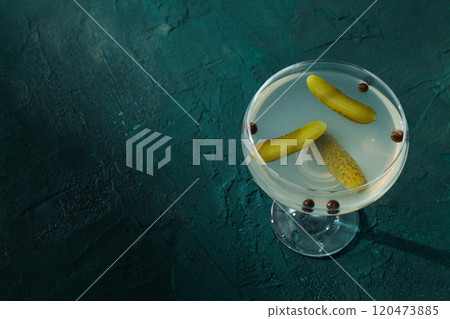 Brine cocktail with pickled cucumber in glass on dark green background, space for text 120473885