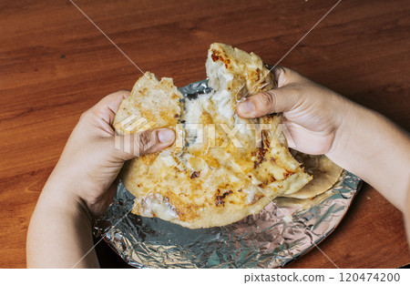 Hands dividing delicious Nicaraguan pupusa on the table, View of hands dividing delicious Salvadoran pupusas on wooden table. Concept of traditional handmade pupusas Hands dividing delicious Nicaraguan pupusa on the table, View of hands dividing delicious Salvadoran pupusas on wooden table. Concept of traditional handmade pupusas 120474200