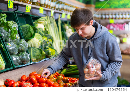 Young guy chooses tomatoes in vegetable shop 120474264